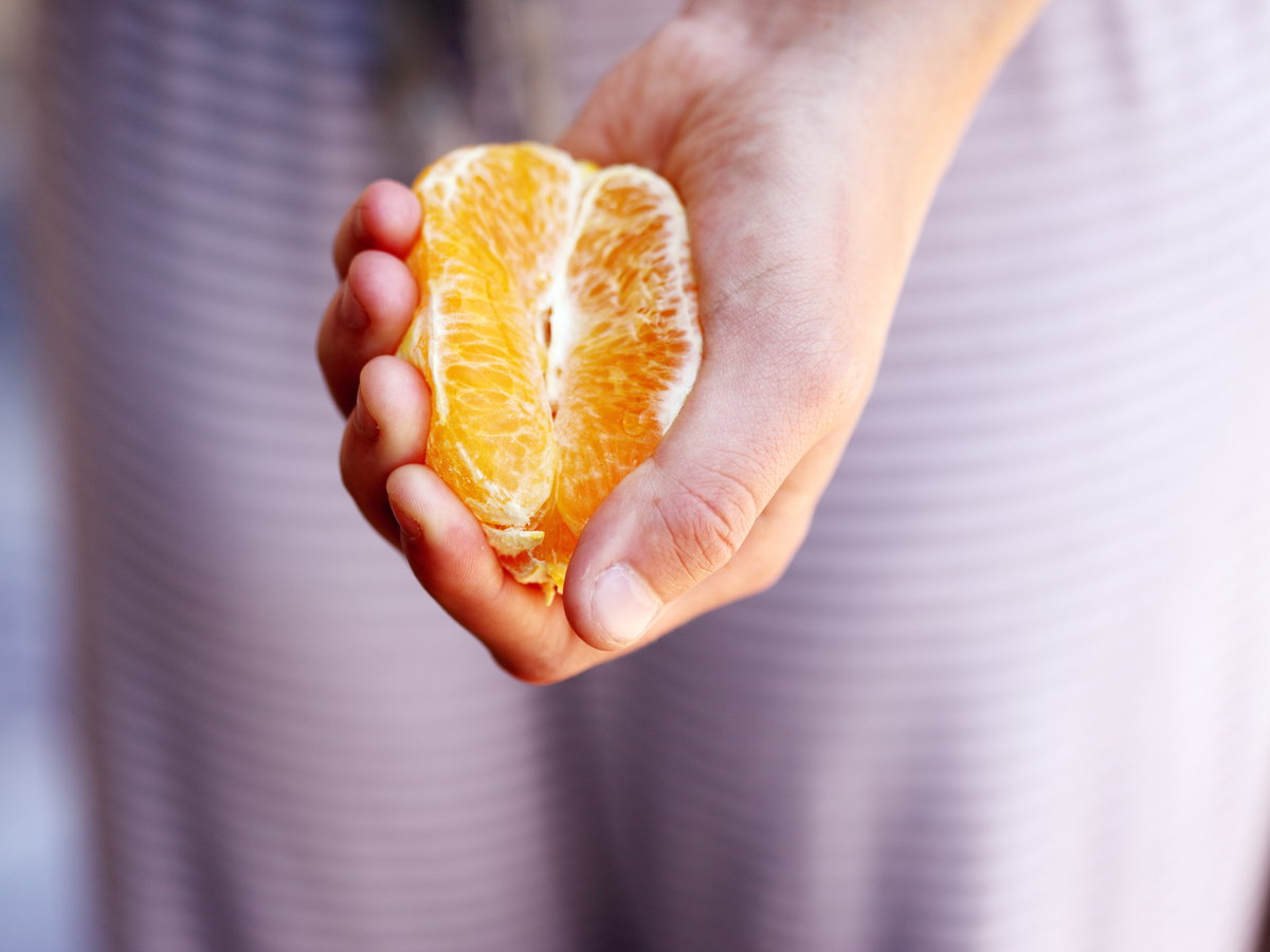 Hand mit Mandarine in der Hand Hälfte davon geschält