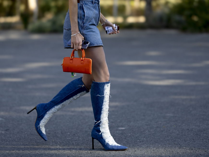 Frau trägt Jeans Stiefel und Jeansrock orangene Tasche Streetstyle