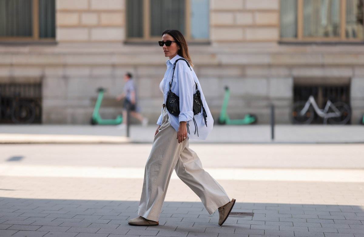 Frau trägt Birkenstocks, eine weiße Bluse und eine Leinenhose