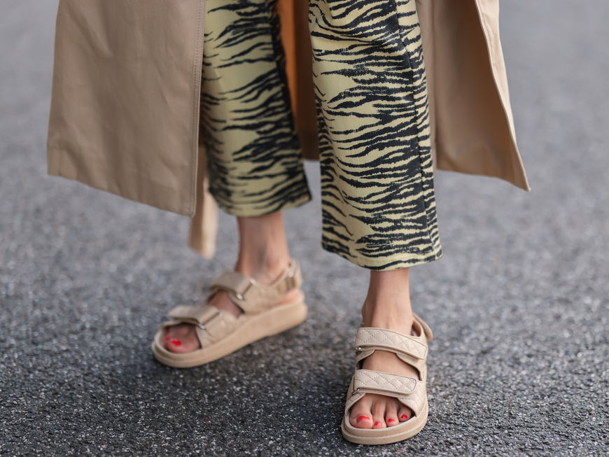 Frau trägt beige Sandalen und eine gemusterte Hose