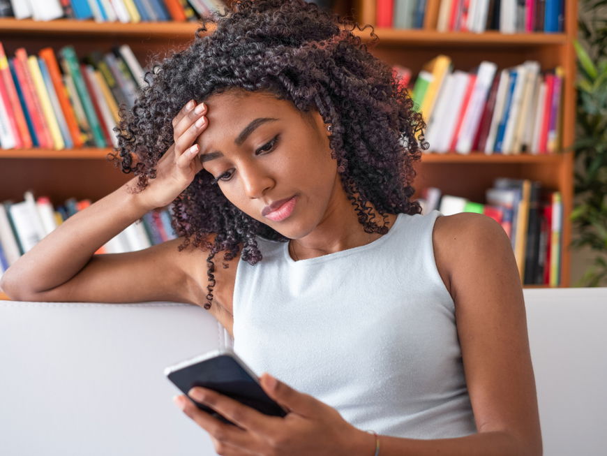 Frau hält Handy zu Hause in der Hand auf dem Sofa