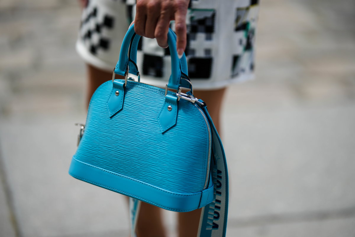 Eine Frau trägt eine türkisfarbene Louis Vuitton Alma Tasche