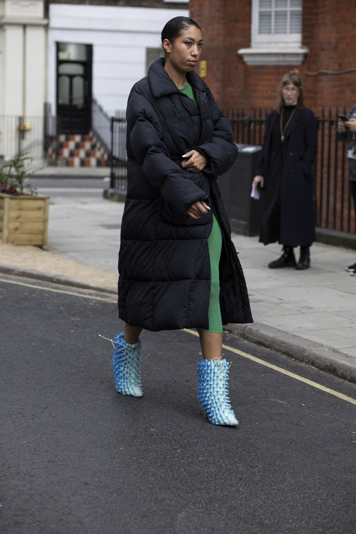 Frau trägt auf London Fashion Week schwarzen wattierten Mantel mit Stiefeletten