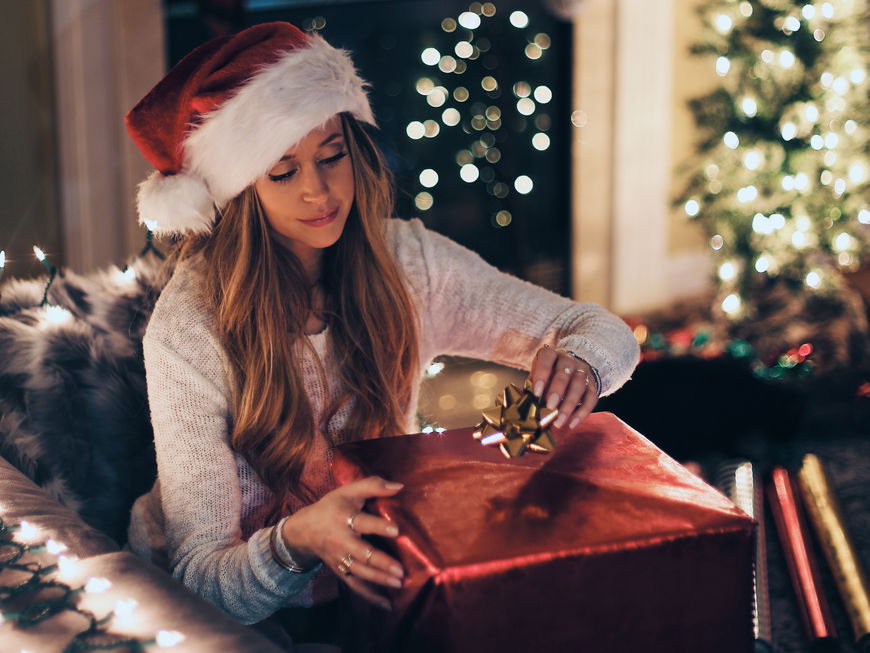 Frau mit Weihnachtsmütze packt ein Geschenk auf dem Sofa ein