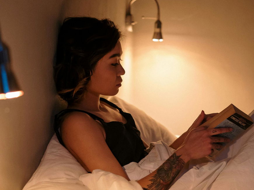 Frau liest im Bett ein Buch.