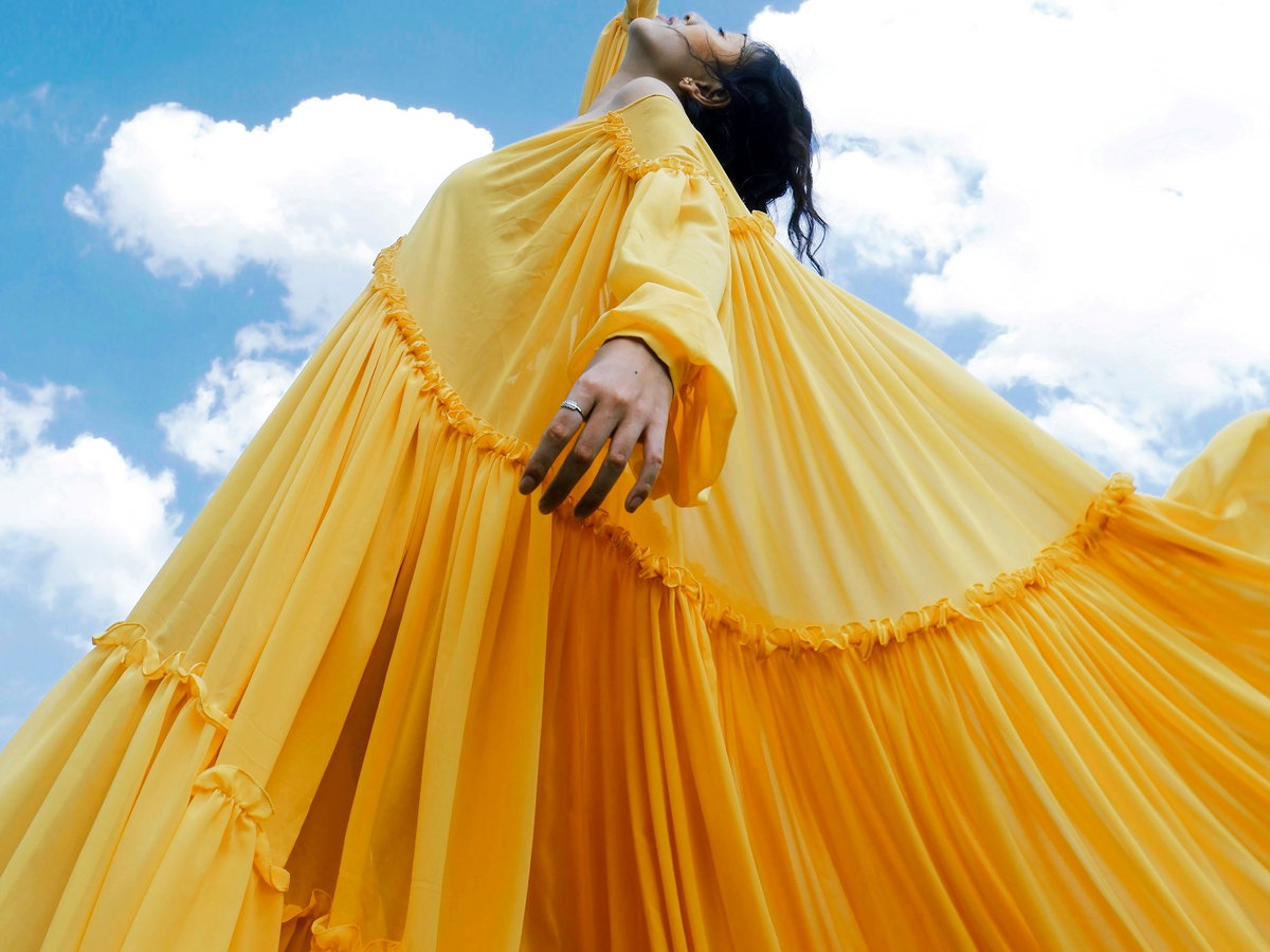 Schwarze Frau in einem gelben Kleid schaut in den blauen Himmel mit Wolken