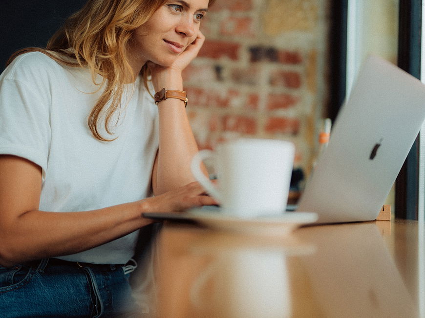 Junge Frau sitzt mit ihrem Laptop in einem Café
