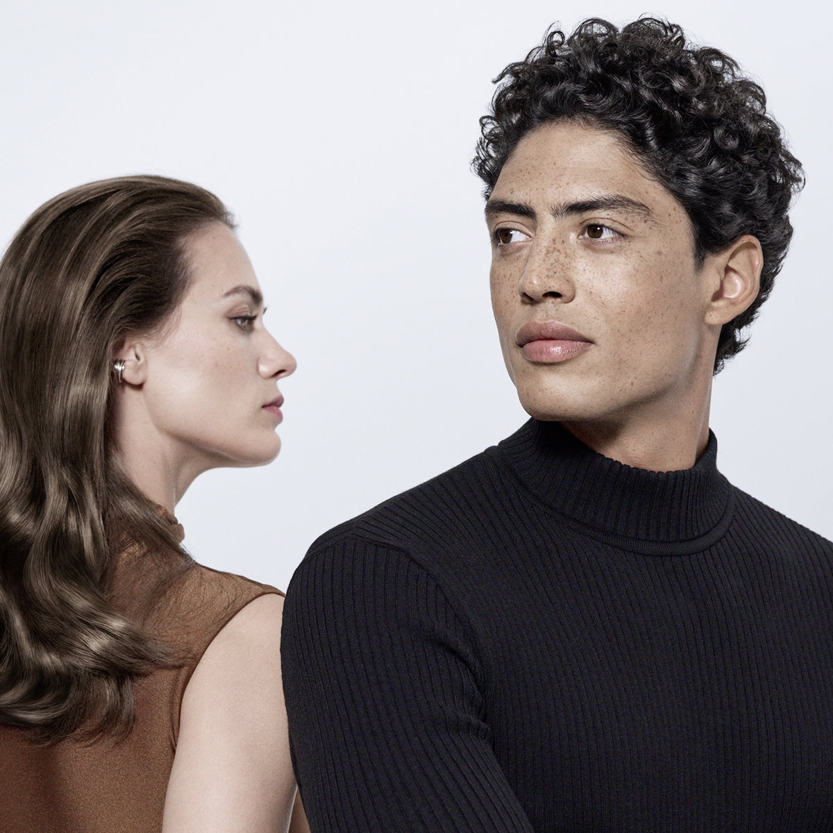 Mann mit braunen Locken und Frau mit braunem langem Haar posieren für das L'Oréal Paris Fiber Booster-Shooting vor hellem Hintergrund.