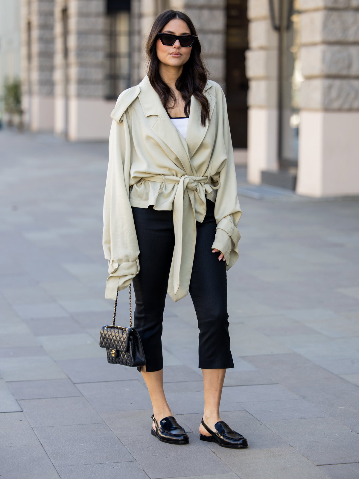 Frau in beiger Trench-Jacke kombiniert mit einer schwarzen Caprihose