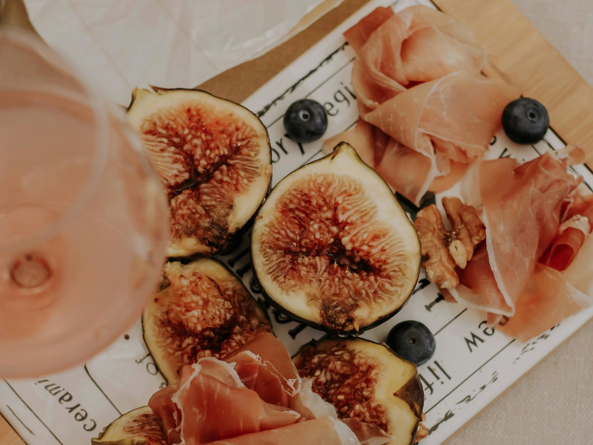 Feigen, Prosciutto und frische Snacks liegen auf einer Servierplatte neben einem sommerlichen Aperitivo-Getränk.