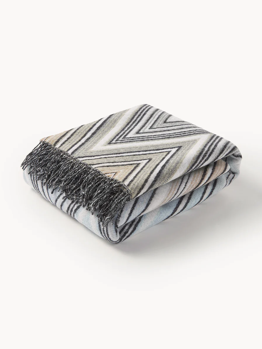 Man gönnt sie sich viel zu selten selbst, dabei ist sie das ultimative Upgrade für jedes Interieur: Die "Plume" Decke aus dem Hause Missoni . Mit ihrem ikonischen Zickzack-Muster und den raffinierten geometrischen Webstrukturen verleiht sie jedem Raum eine beeindruckende optische Tiefe. Gefertigt in Italien, bestechen die filigranen Linien und die edlen Fransen durch höchste Handwerkskunst. Ob lässig über das Sofa drapiert oder als Akzent auf dem Sessel – dieses hochwertige Piece vereint Funktionalität mit High-Fashion-Flair und macht das gemeinsame Zuhause sofort zum stilvollen Rückzugsort.